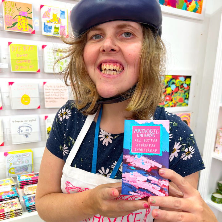 Artist holding bright coloured box of Sunshine at the Seaside, All Butter Hebridean Shortbread