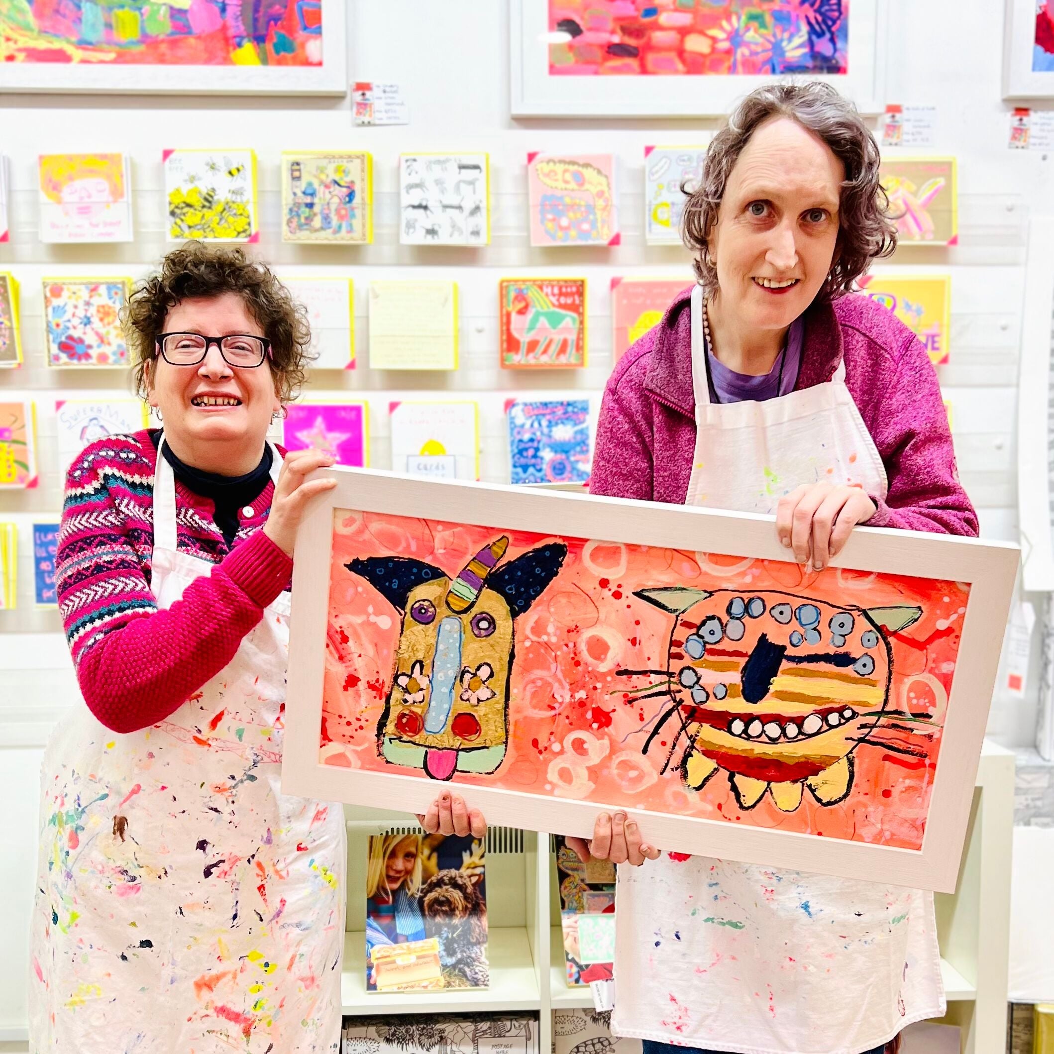 Two female artists holding Framed painting of bright coloured unicorn and tiger