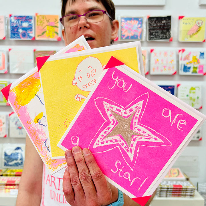 A female artist holding 3 cards focusing on A pink and gold card with a hand drawn star and the words you are a star!