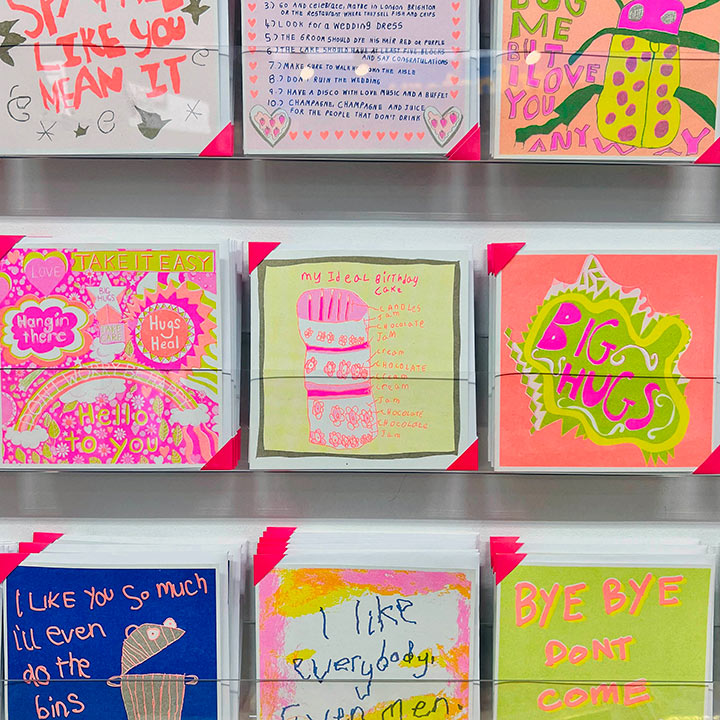 A card rack focusing on A pink, yellow and gold card with a hand drawn birthday cake and the words my ideal birthday cake 