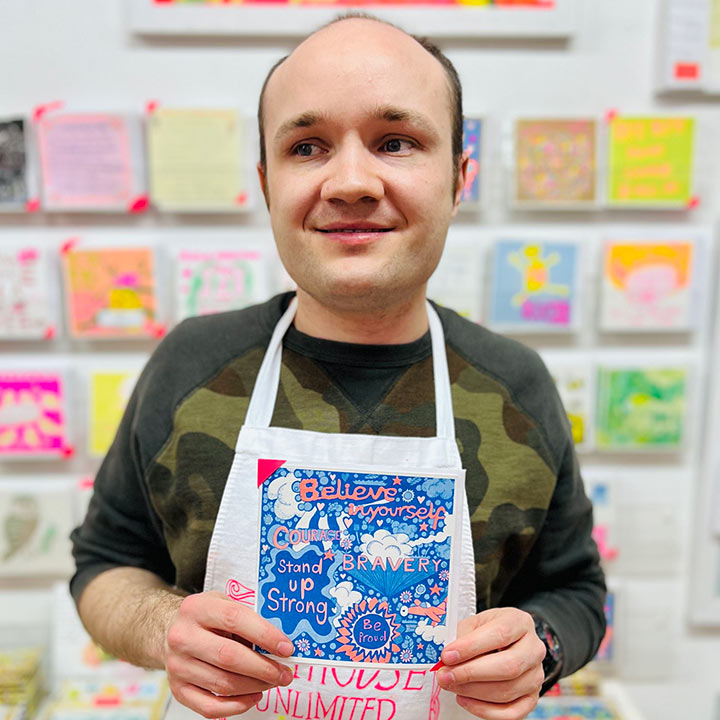 Male artist holding A blue and orange card with uplifting messages hand drawn onto it such as Believe in your self and bravery 