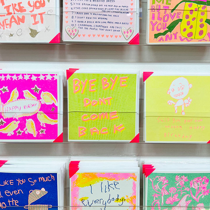 Cards on a rack focusing on Bright neon green card with the words in orange 'Bye Bye Don't Come Back"