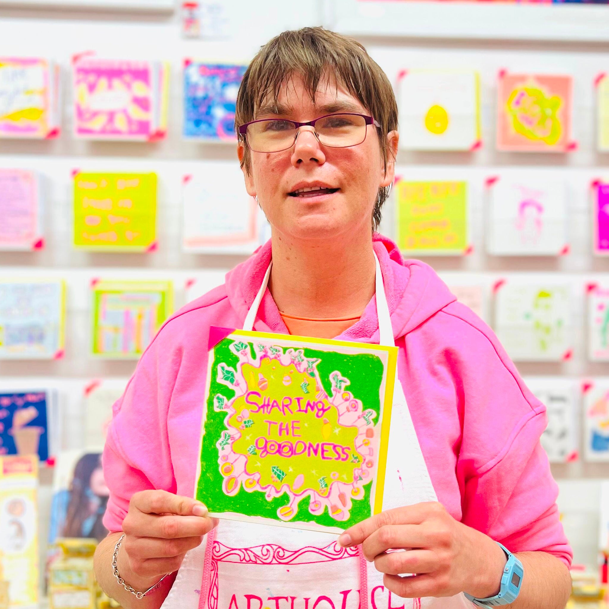 A female artist holding A hand drawn pink and green card with the words sharing the goodness