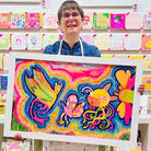 Female artist holding A framed bright coloured painting of strange creatures called Flying Fun with the Friends in the Field