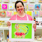 Female artist holding a framed painting of a green, yellow and pink caterpillar