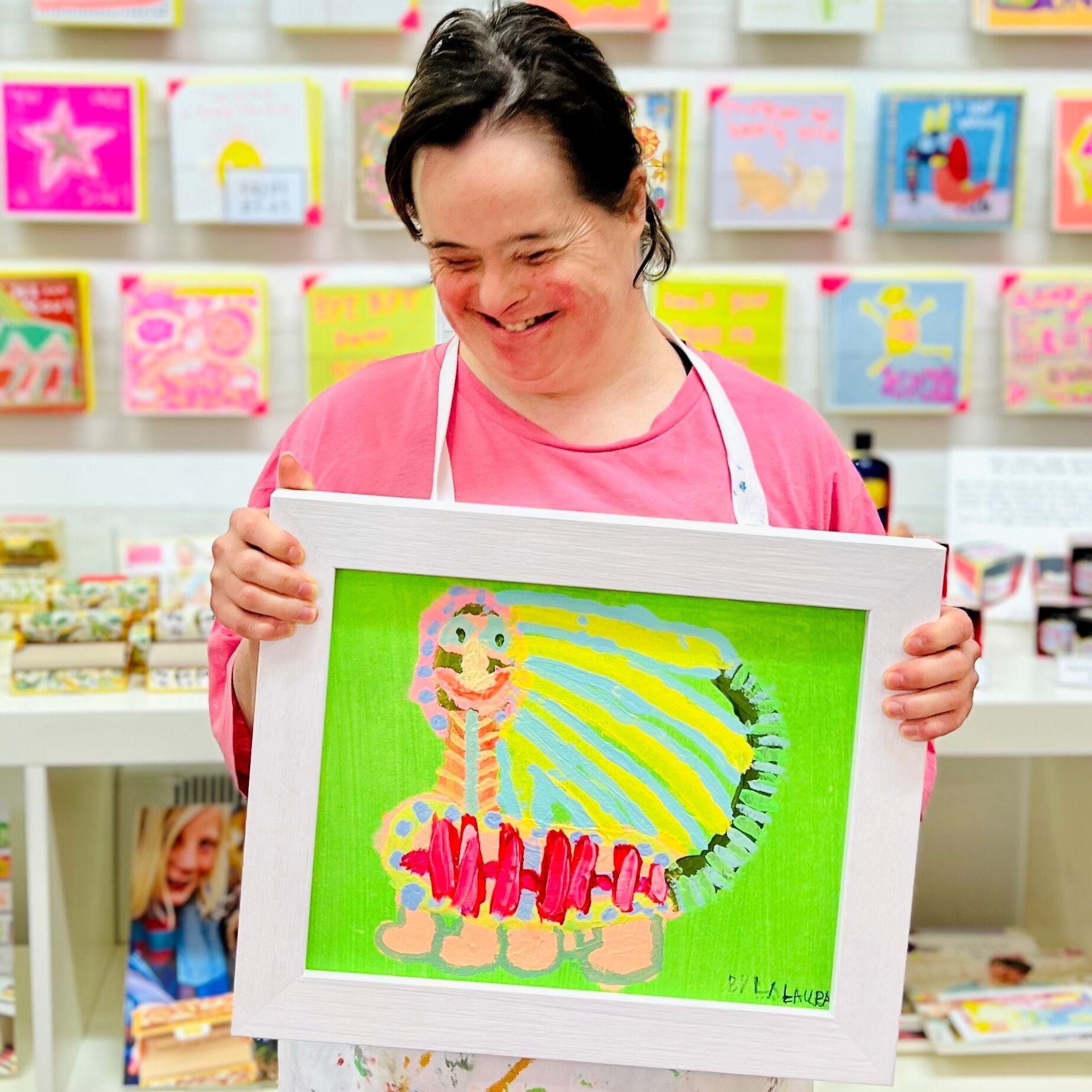 Female artist holding a framed painting of a green, yellow and pink caterpillar