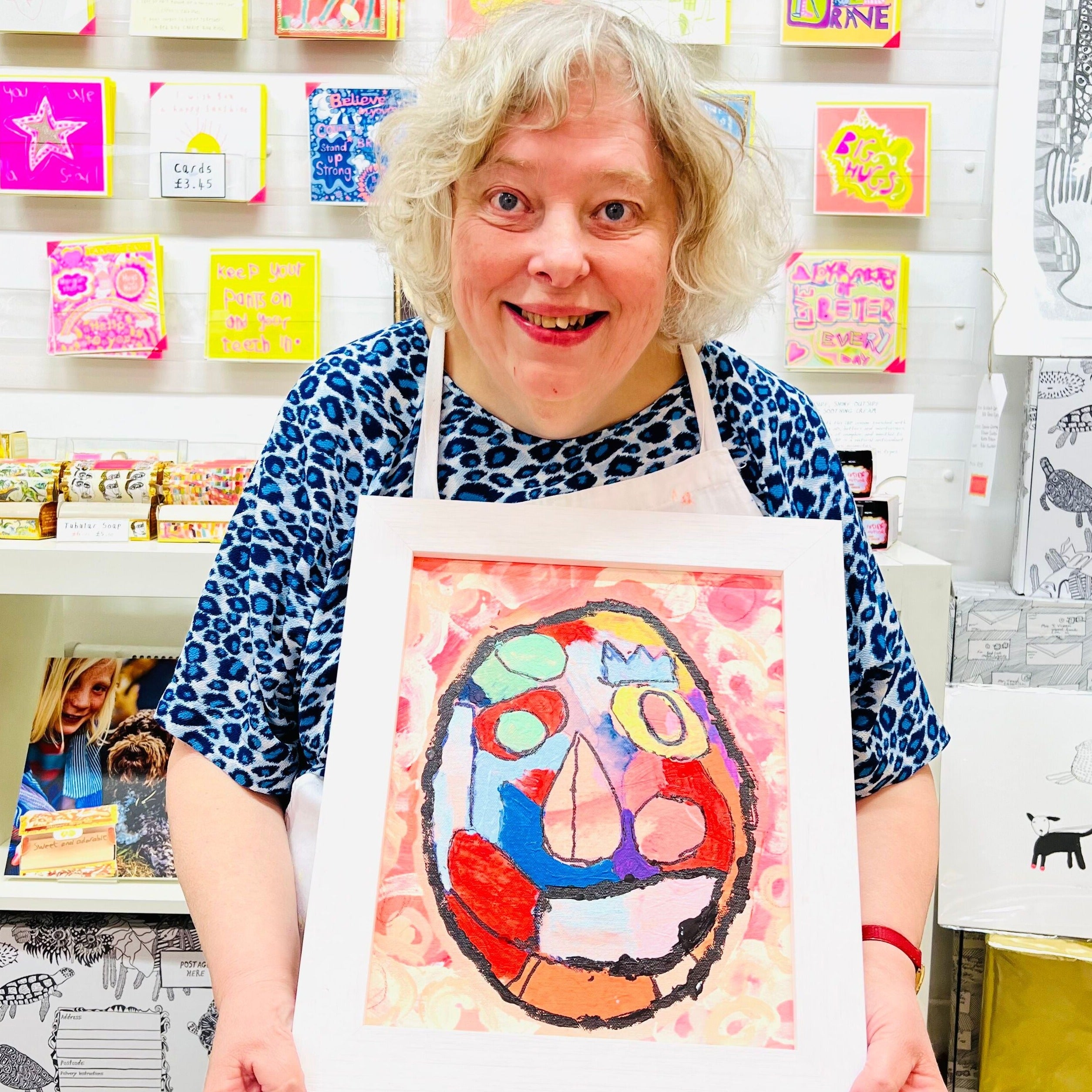 Female artist holding Framed painting of a bright coloured mask 