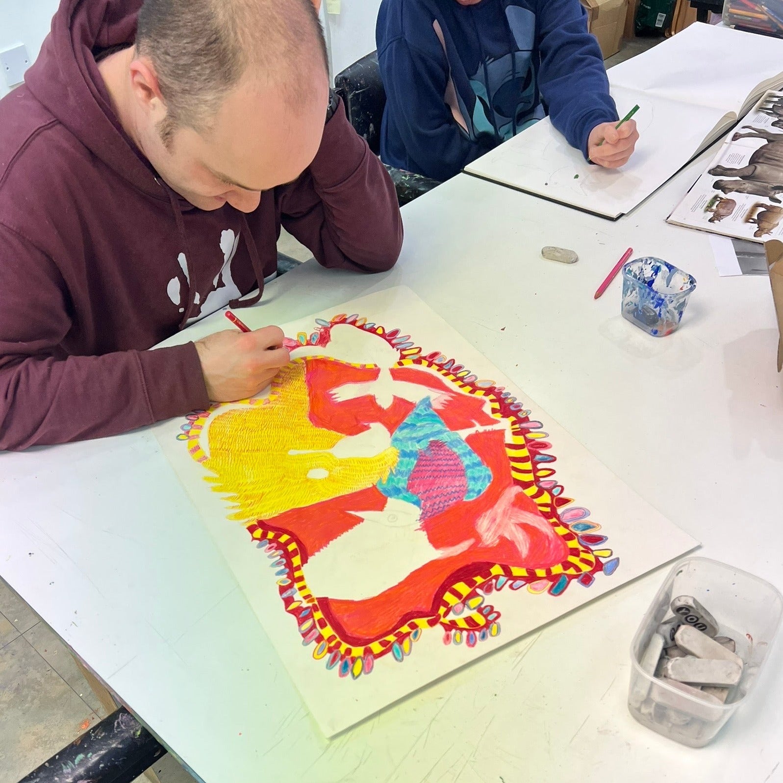 Male artist in a studio drawing bright coloured birds in pencil