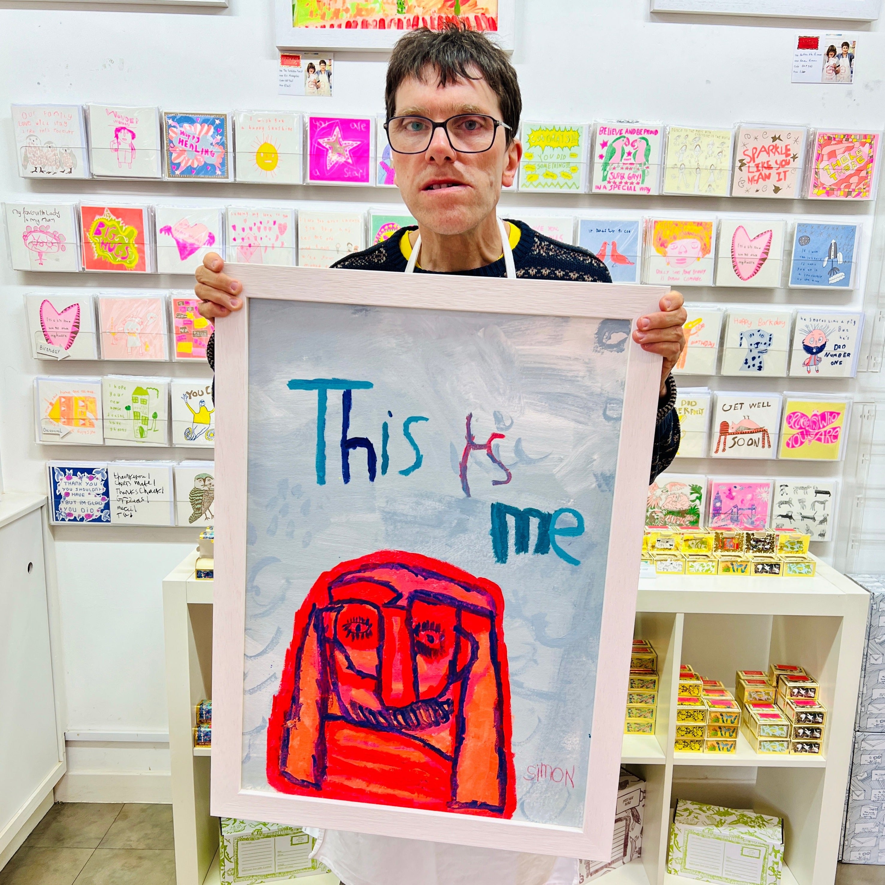 Male artist holding Framed painted image of a red character with the words This is Me above
