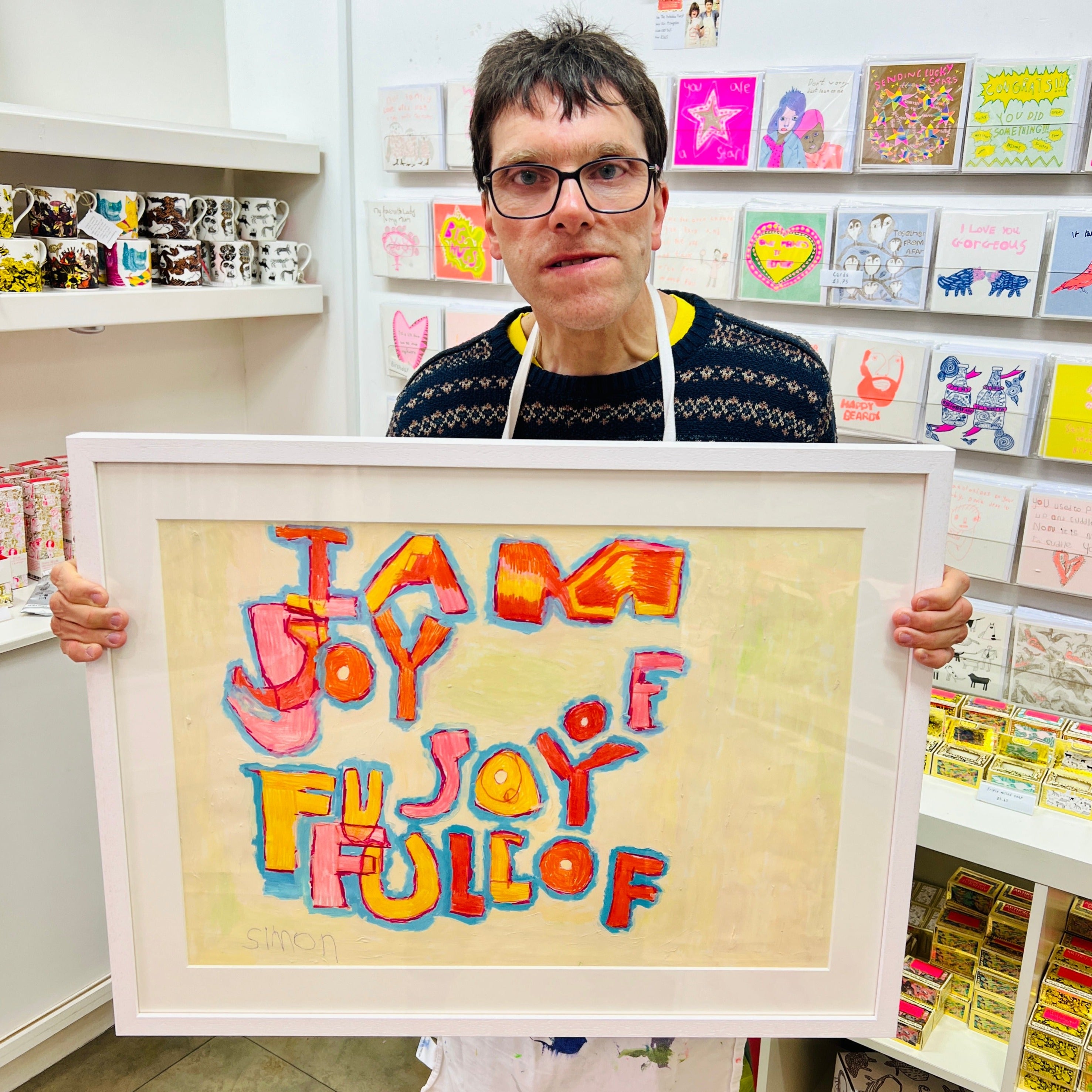 Male artist holding Framed painting of the words 'I am full of joy"