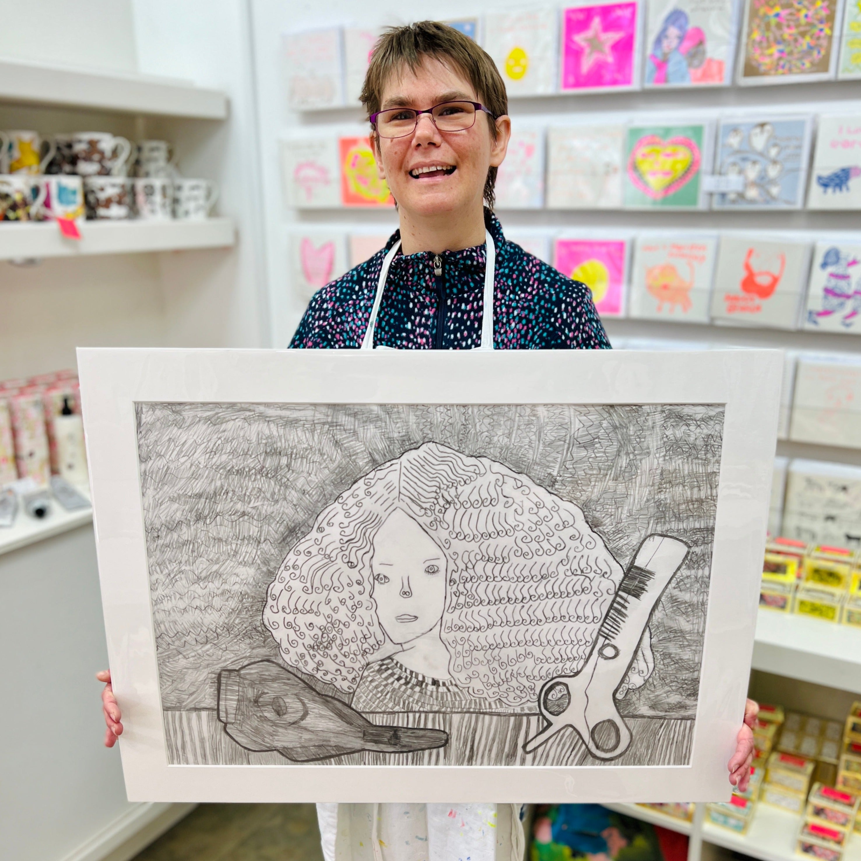 Female artist holding Hand drawn picture in pencil of a woman with large hair and scissors 