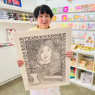 Female artist holding A hand drawn picture in pencil of a woman in front of a mirror with two hair brushes