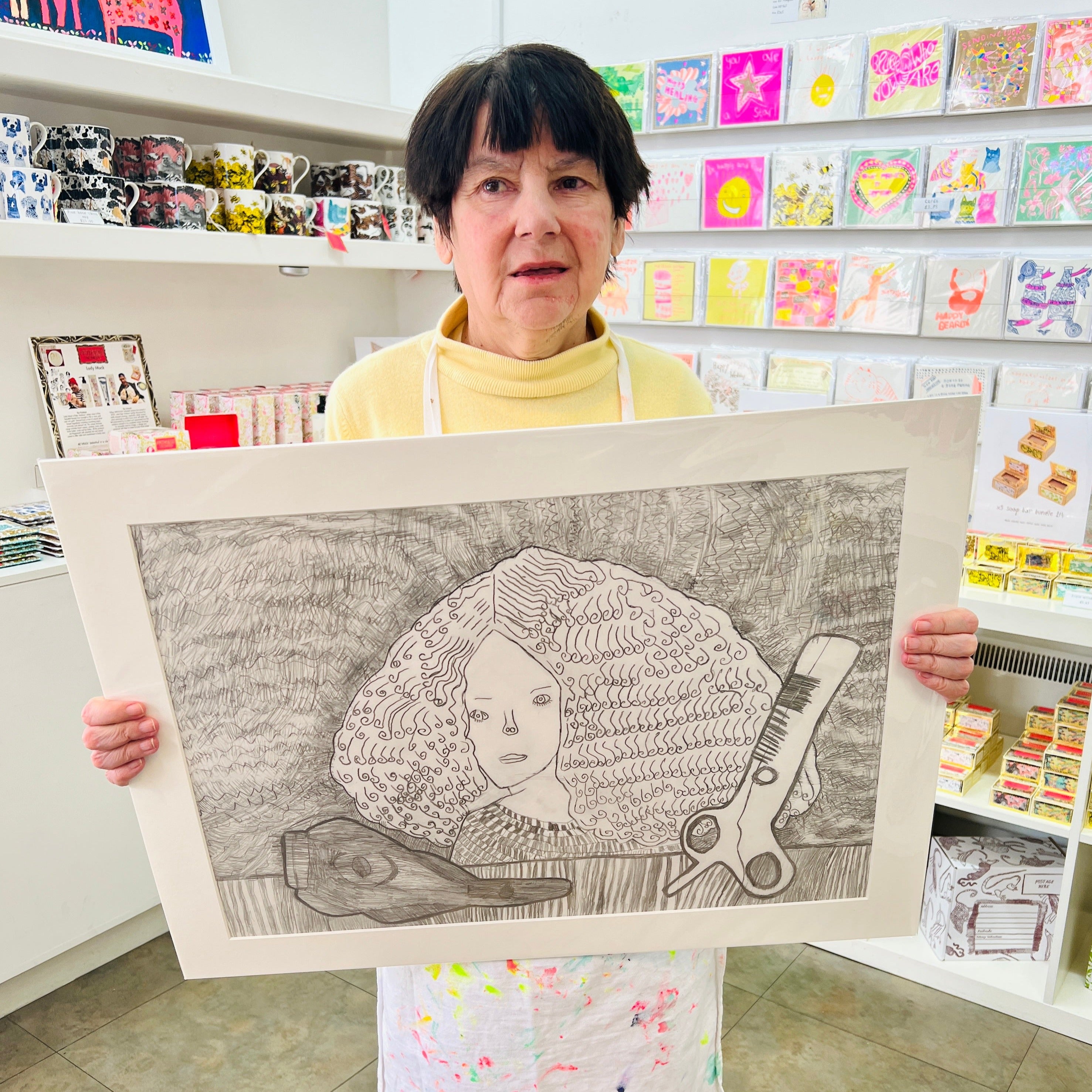 Female artist holding Hand drawn picture in pencil of a woman with large hair and scissors