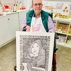 Male artist holding A hand drawn picture in pencil of a woman in front of a mirror with two hair brushes
