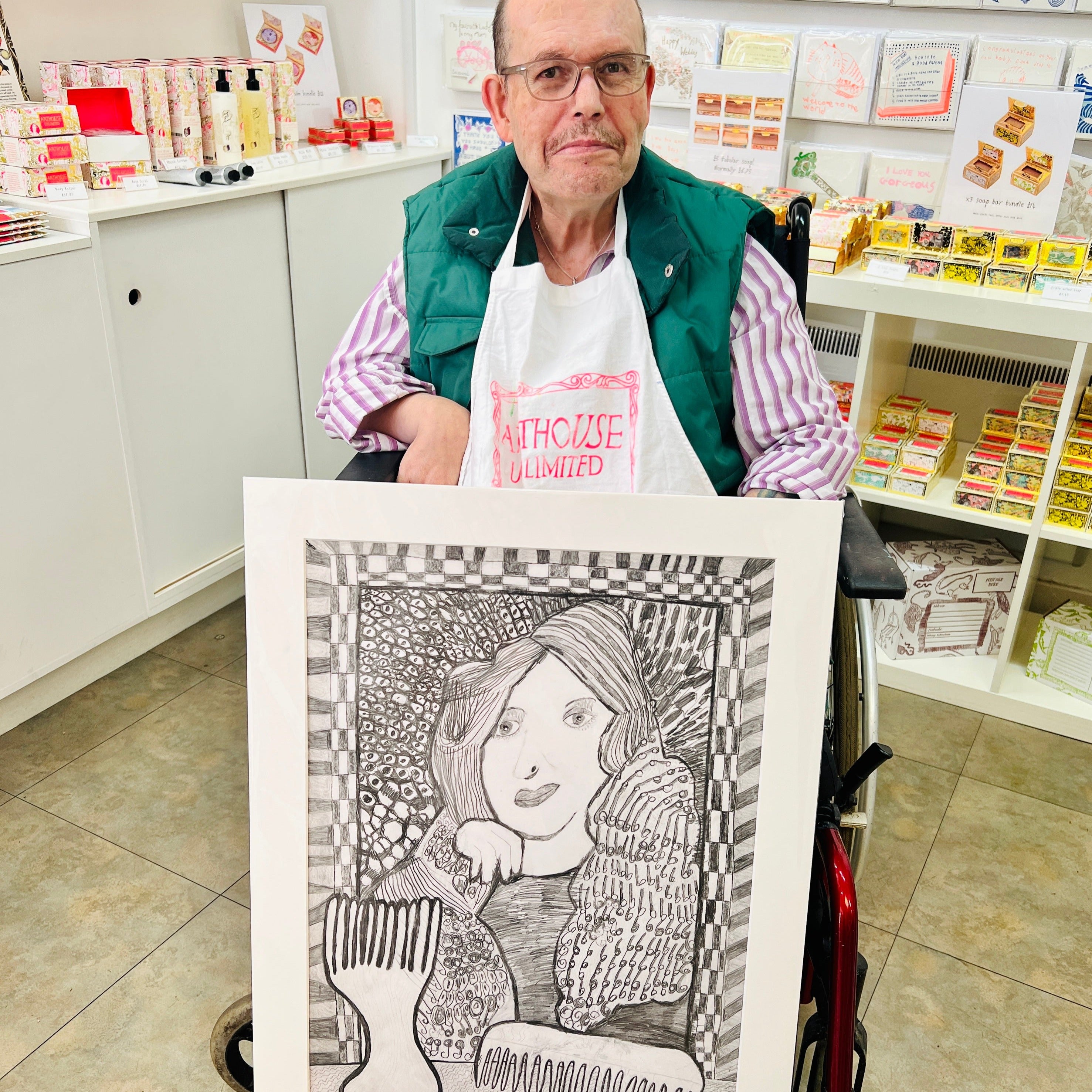 Male artist holding A hand drawn picture in pencil of a woman in front of a mirror with two hair brushes