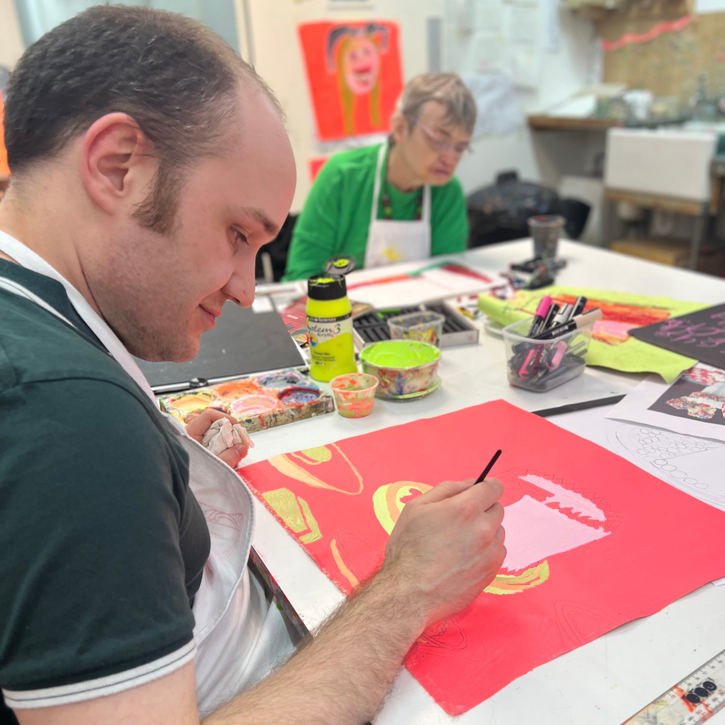 Male artist in a studio painting a bright coloured celebration cake 