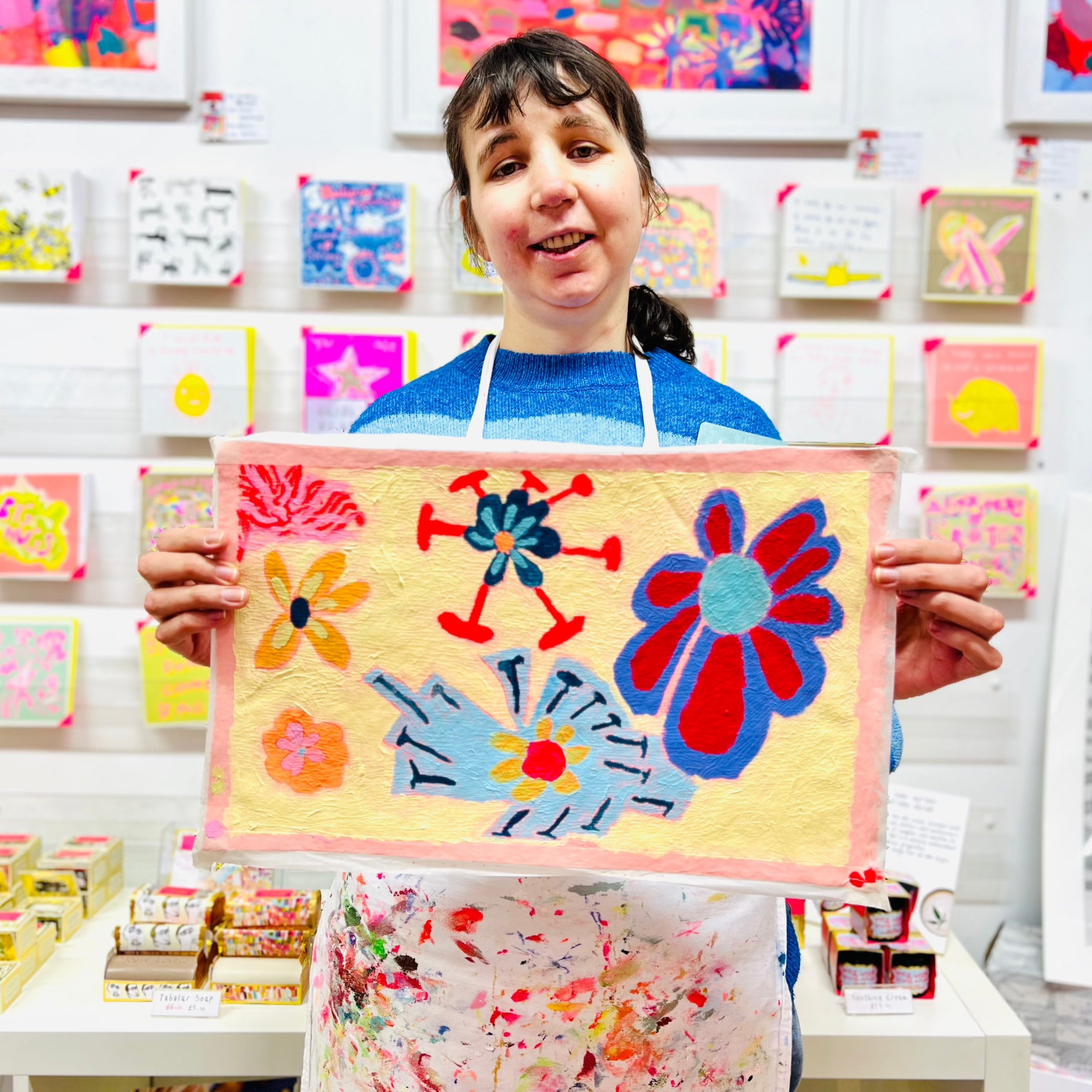 Female artist holding Framed painting of flowers in blues, purples and yellow