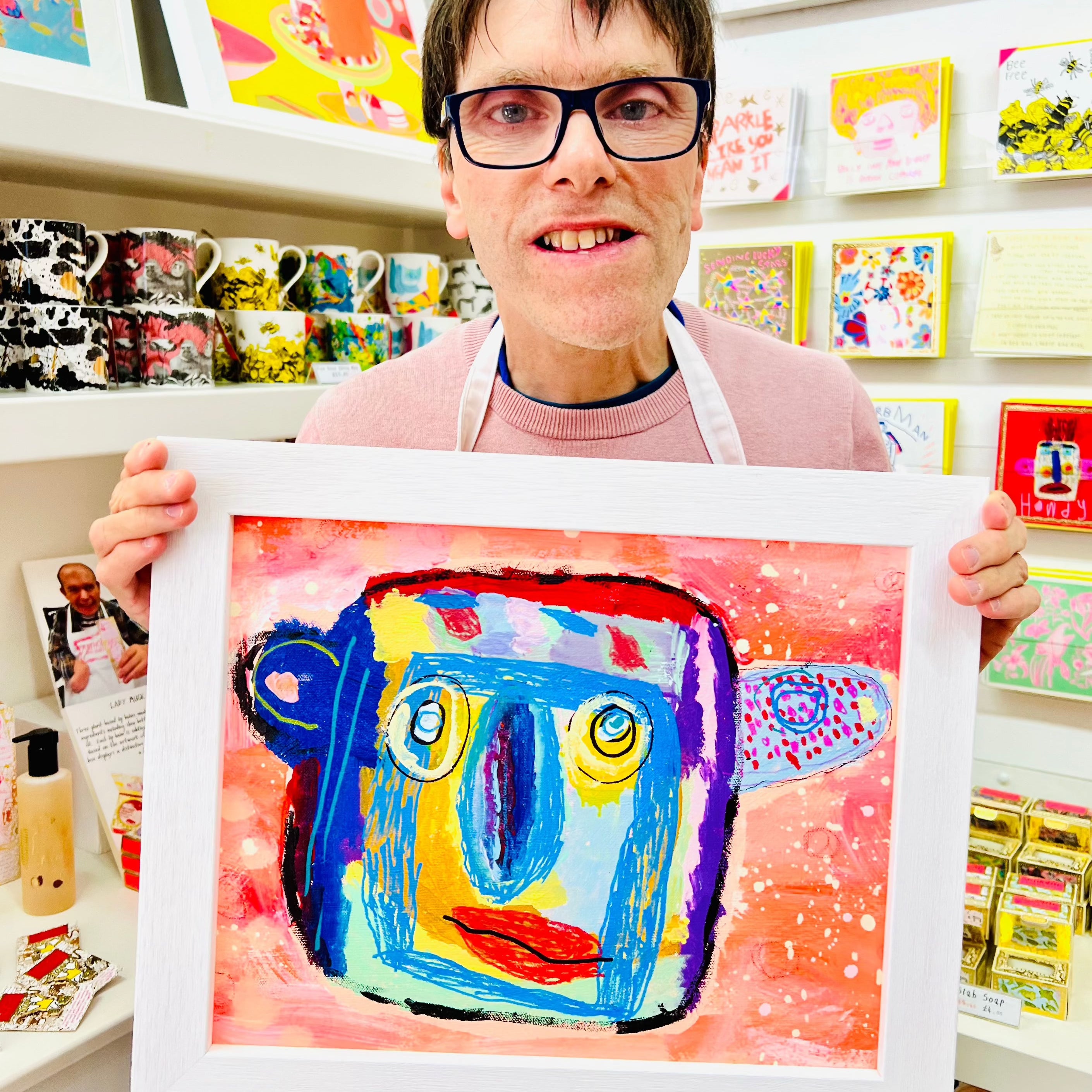 Male artist holding Framed abstract painting of a man with a blue face and large ears and nose