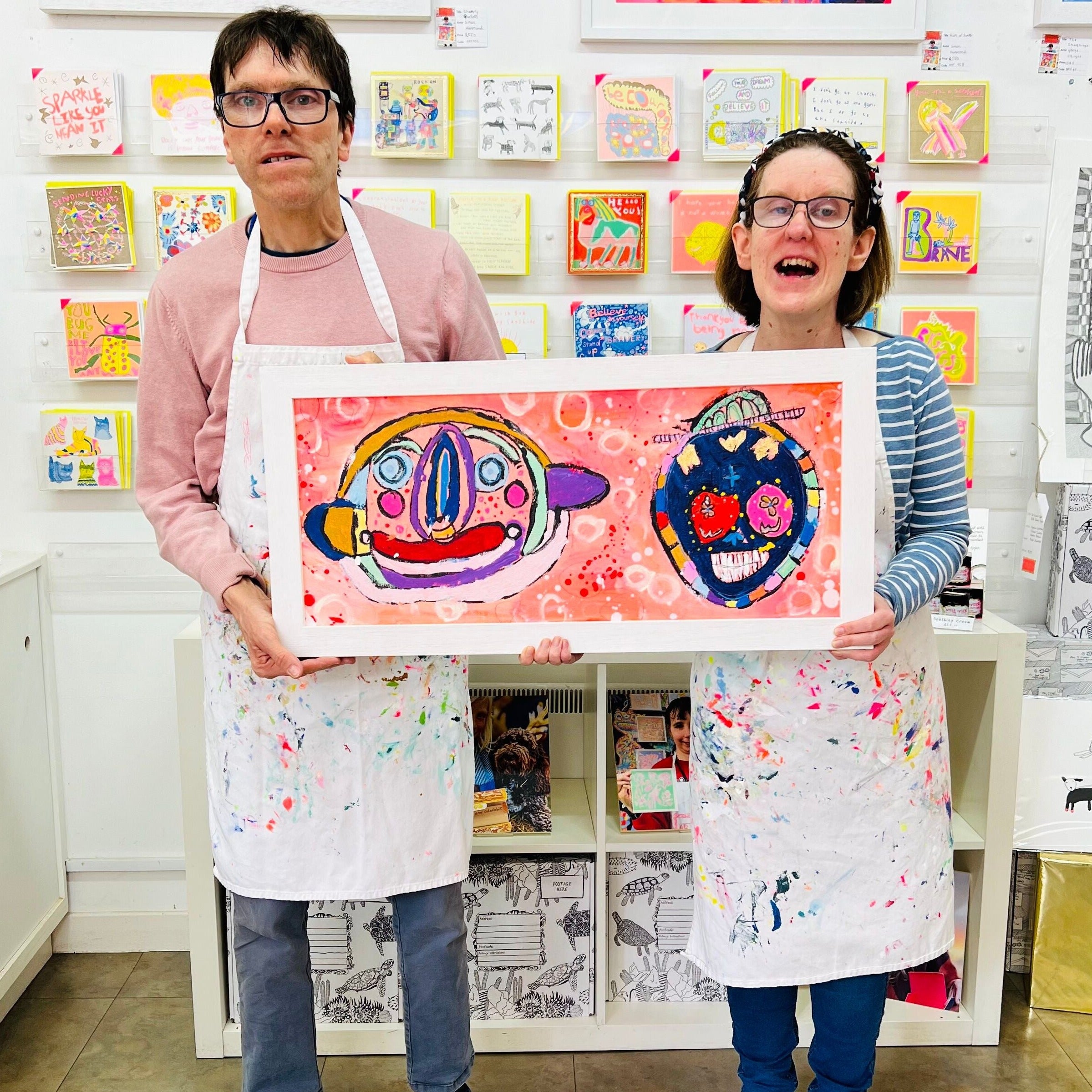 male and female artist holding Framed colourful abstract painting of two characters in bright colours
