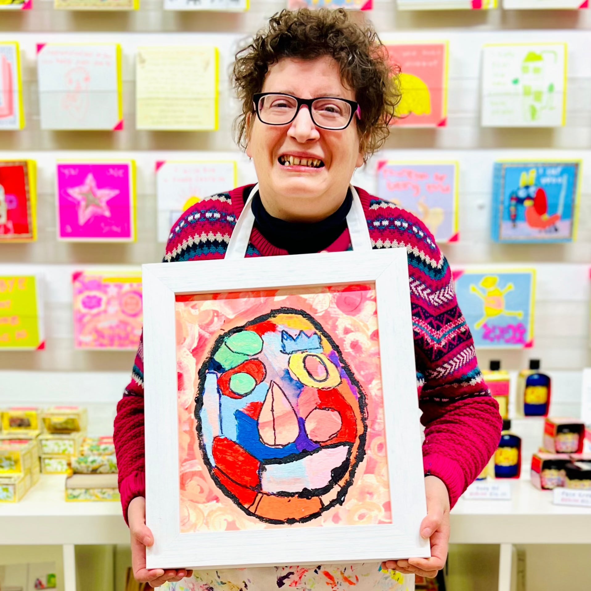 female artist holding Framed painting of a bright coloured mask 