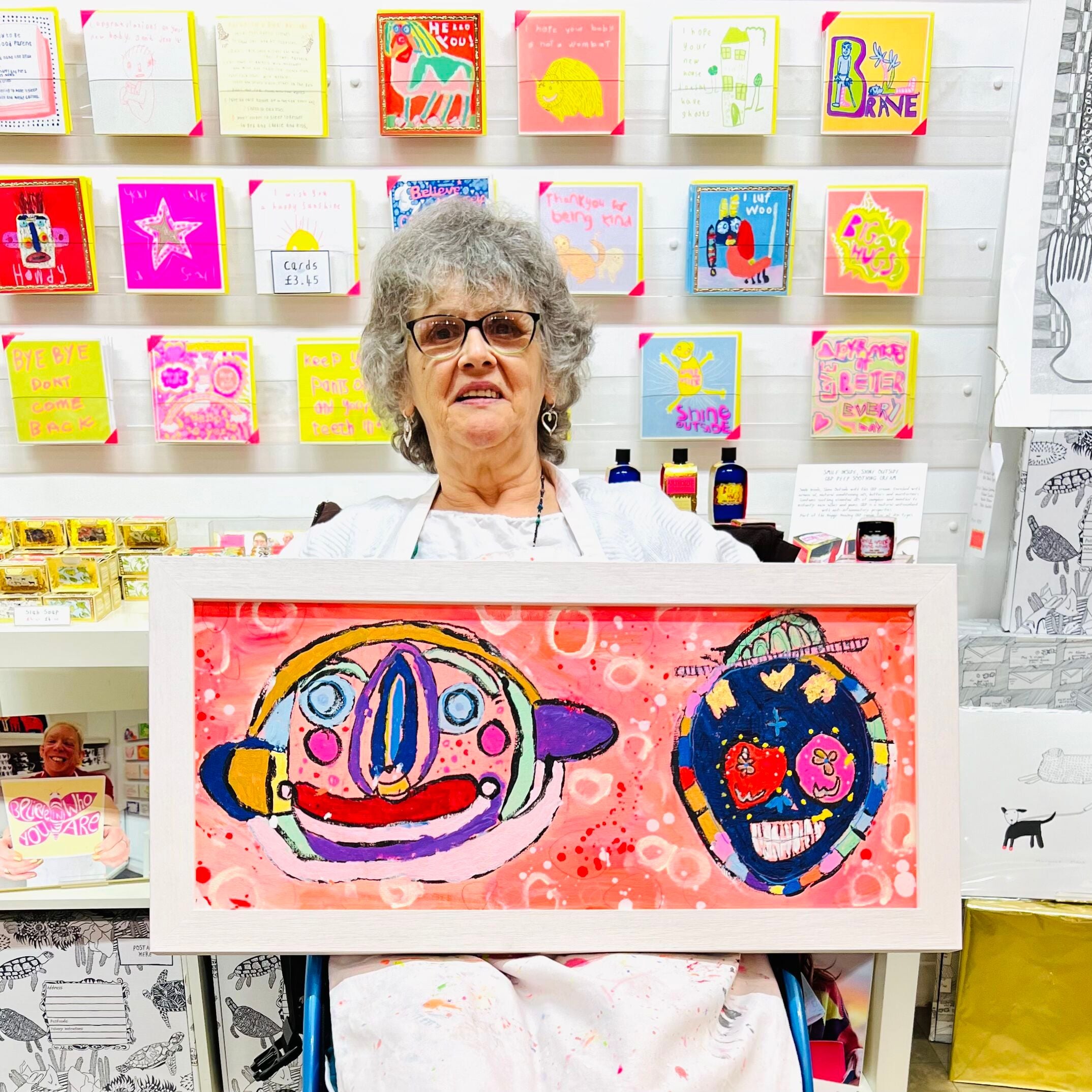 Female artist holding Framed colourful abstract painting of two characters in bright colours