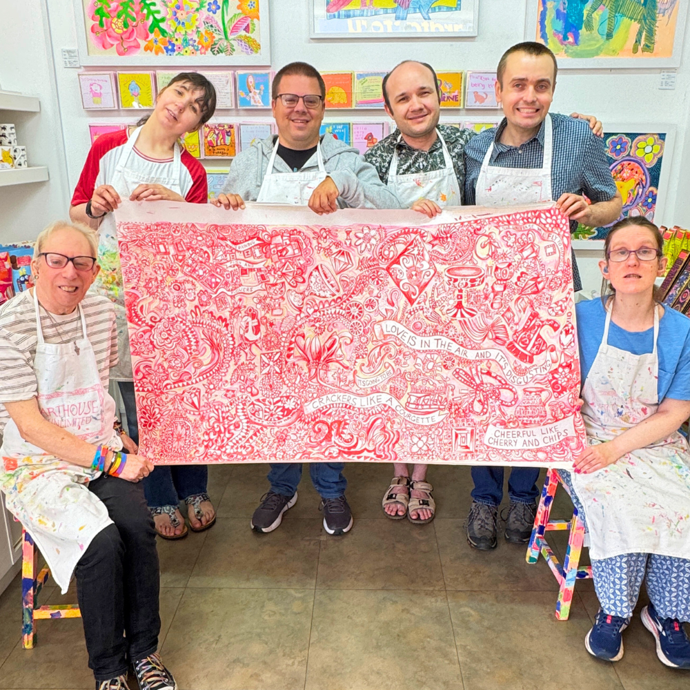 Group of people holding a large red and white patterned artwork in an art studio.
