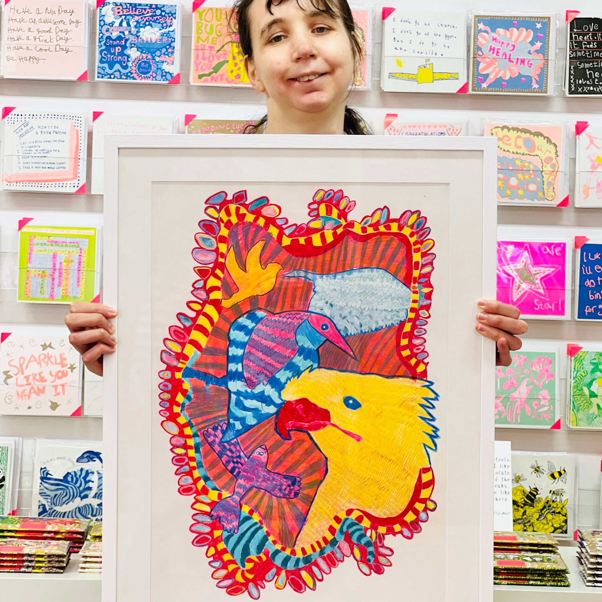 Female artist holding Framed painting of blue, pink and yellow birds 