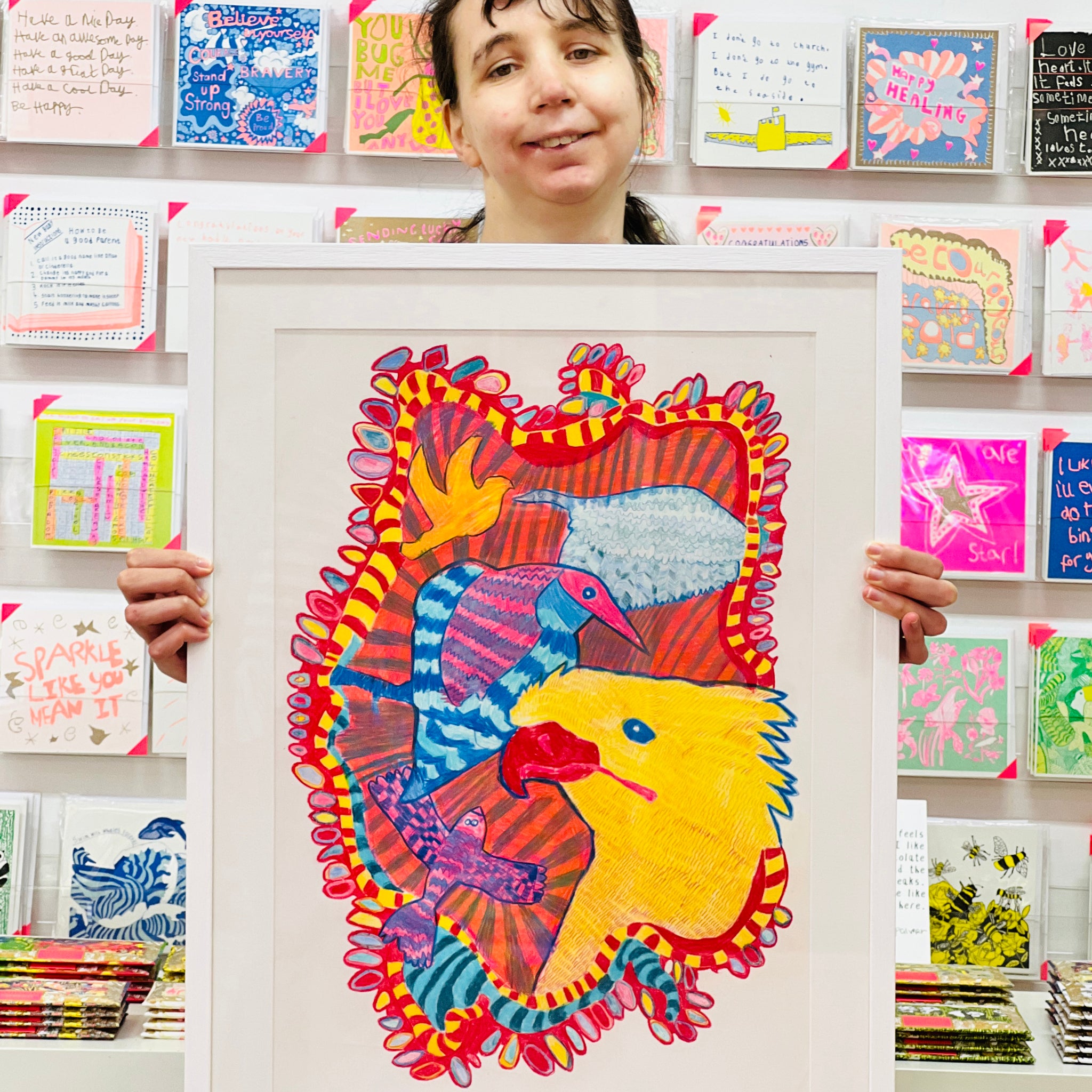 Female artist holding Framed painting of blue, pink and yellow birds