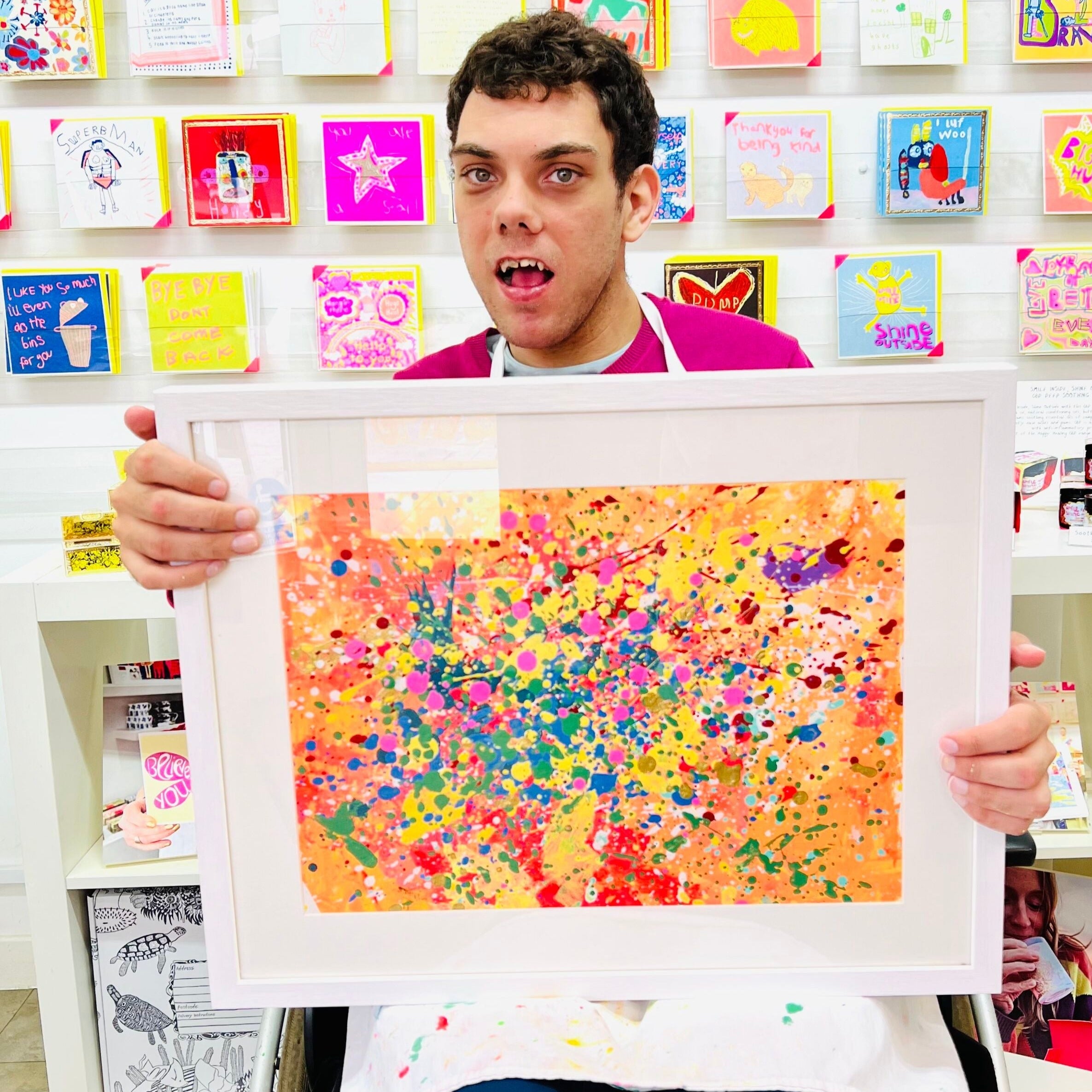 Male artist holding Framed colour painting of pink, orange and yellow splats