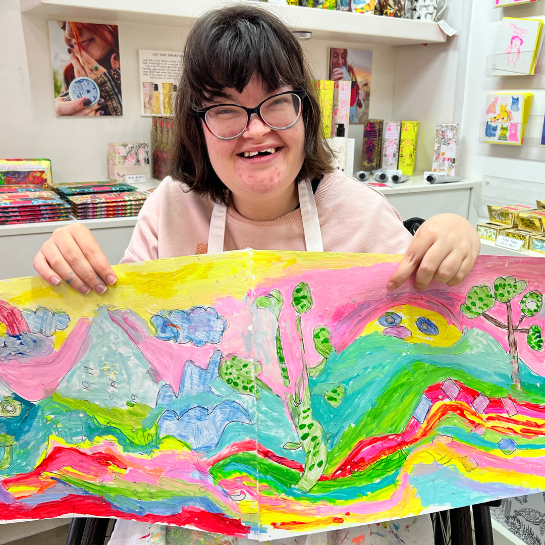 female artist holding Framed bright coloured painting of a landscape