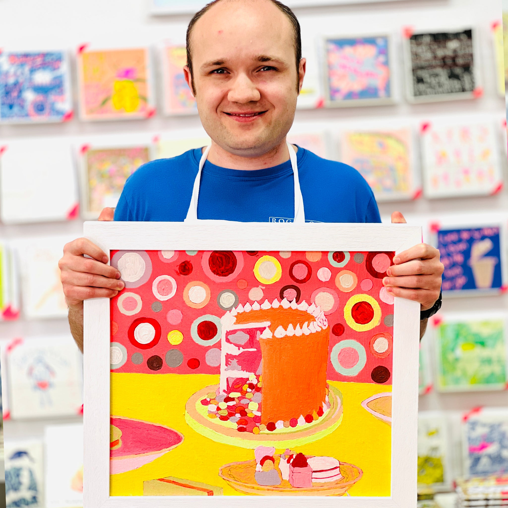 Male artist holding Framed hand painted celebration cake in pinks, oranges and yellow