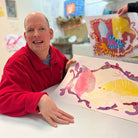 Male artist in a studio drawing bright coloured birds in pencil  