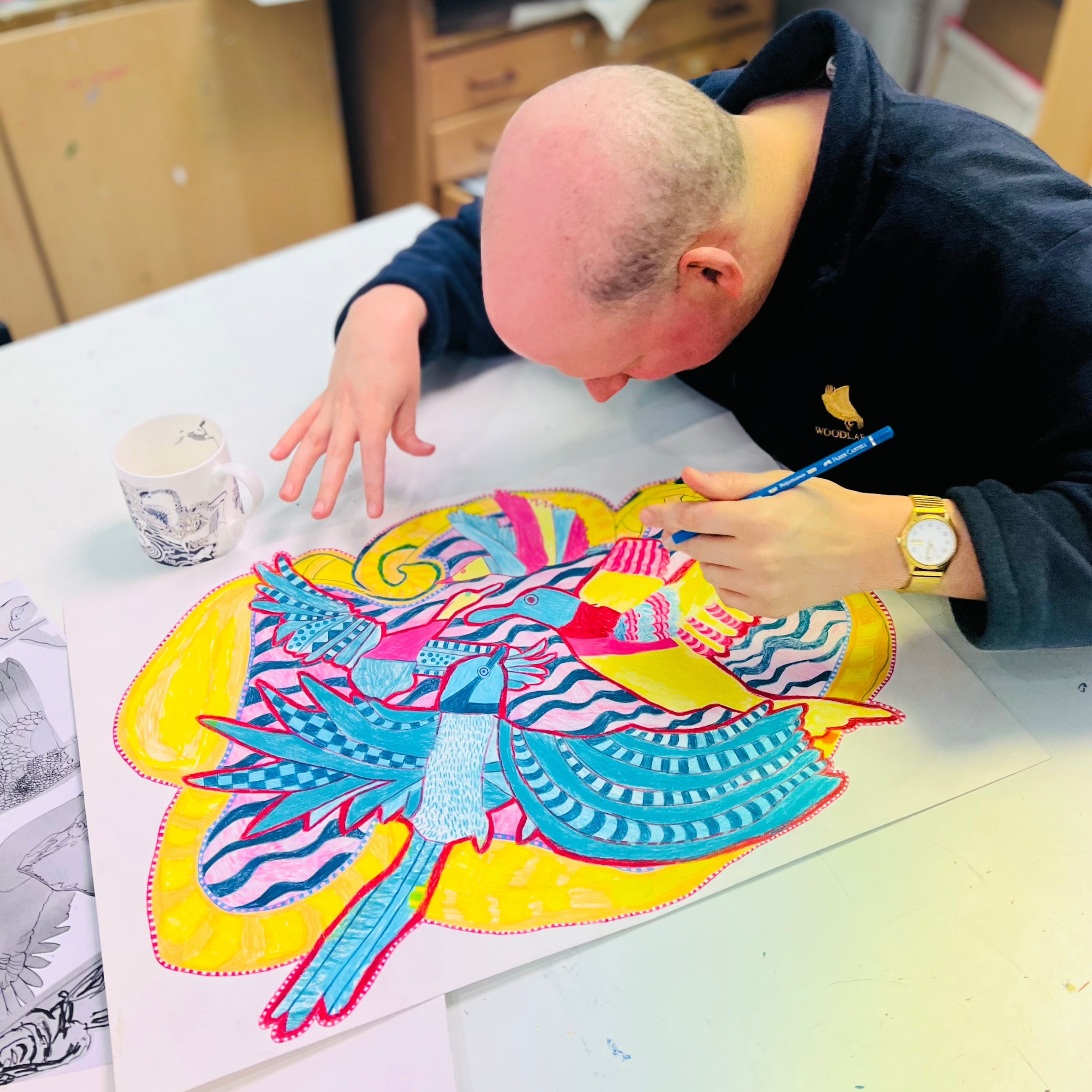 Male artist in a studio drawing bright coloured birds with pencil