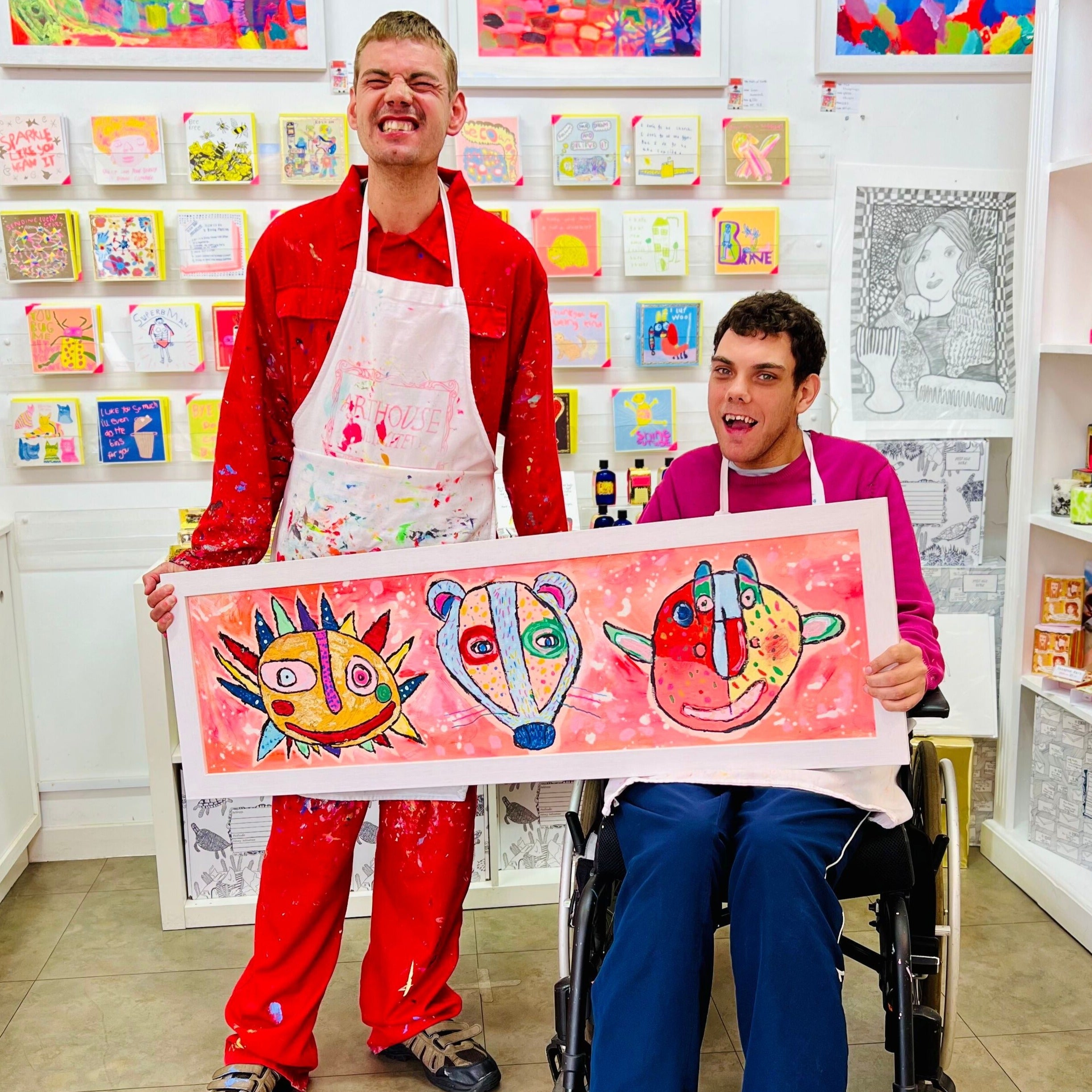 2 male artists holding Framed colourful artwork of an abstract sun, badger and a man