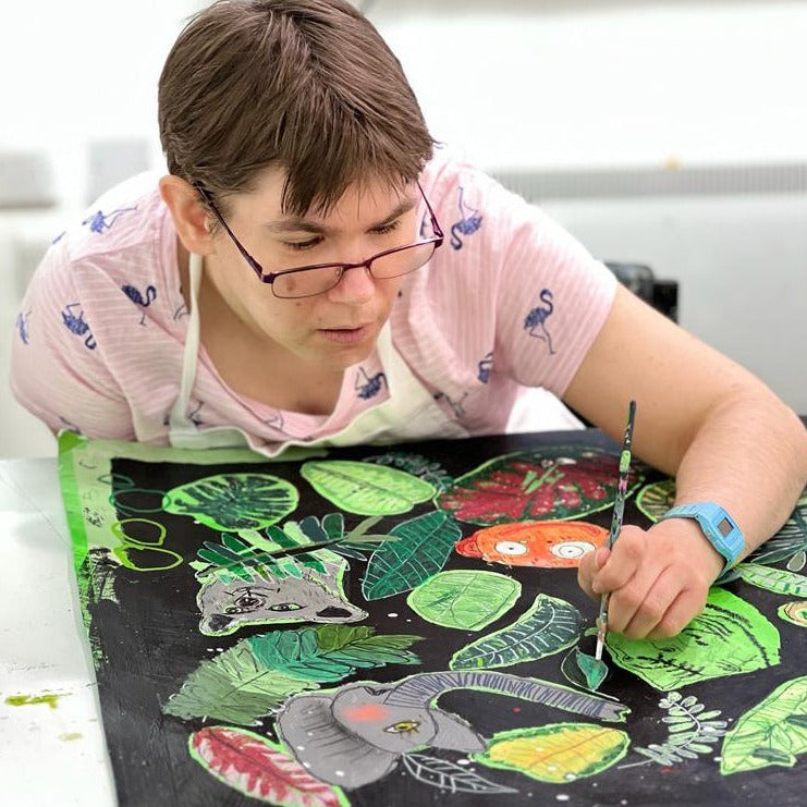 Female artist painting a bright coloured jungle scene 