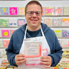 A male artist holding A blue and orange card with a hand drawn book with a list of how to be a good parent 