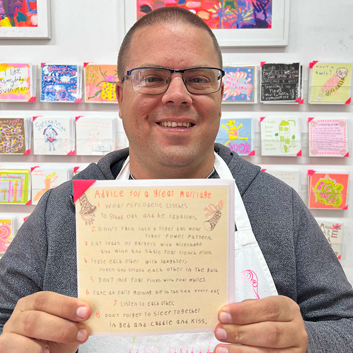 A male artist holding A yellow and orange card with a hand drawn list of  advice for a great marriage 