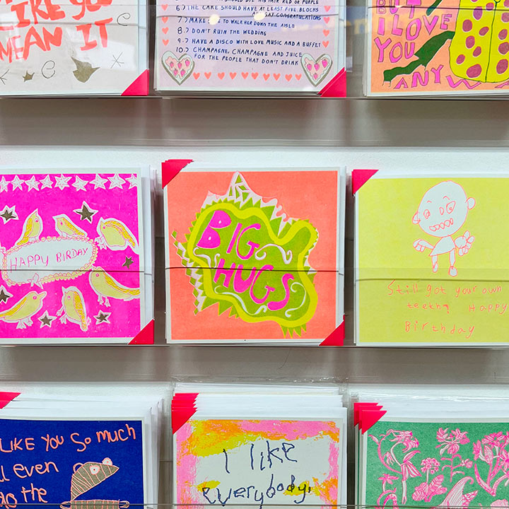 A card rack focusing on An orange, green and pink hand drawn card with the words big hugs