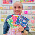 Male artist holding 3 cards focusing on A blue and orange card with uplifting messages hand drawn onto it such as Believe in your self and bravery 