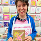 A female artist holding A gold, pink and orange hand drawn character with the words you are a superstar 