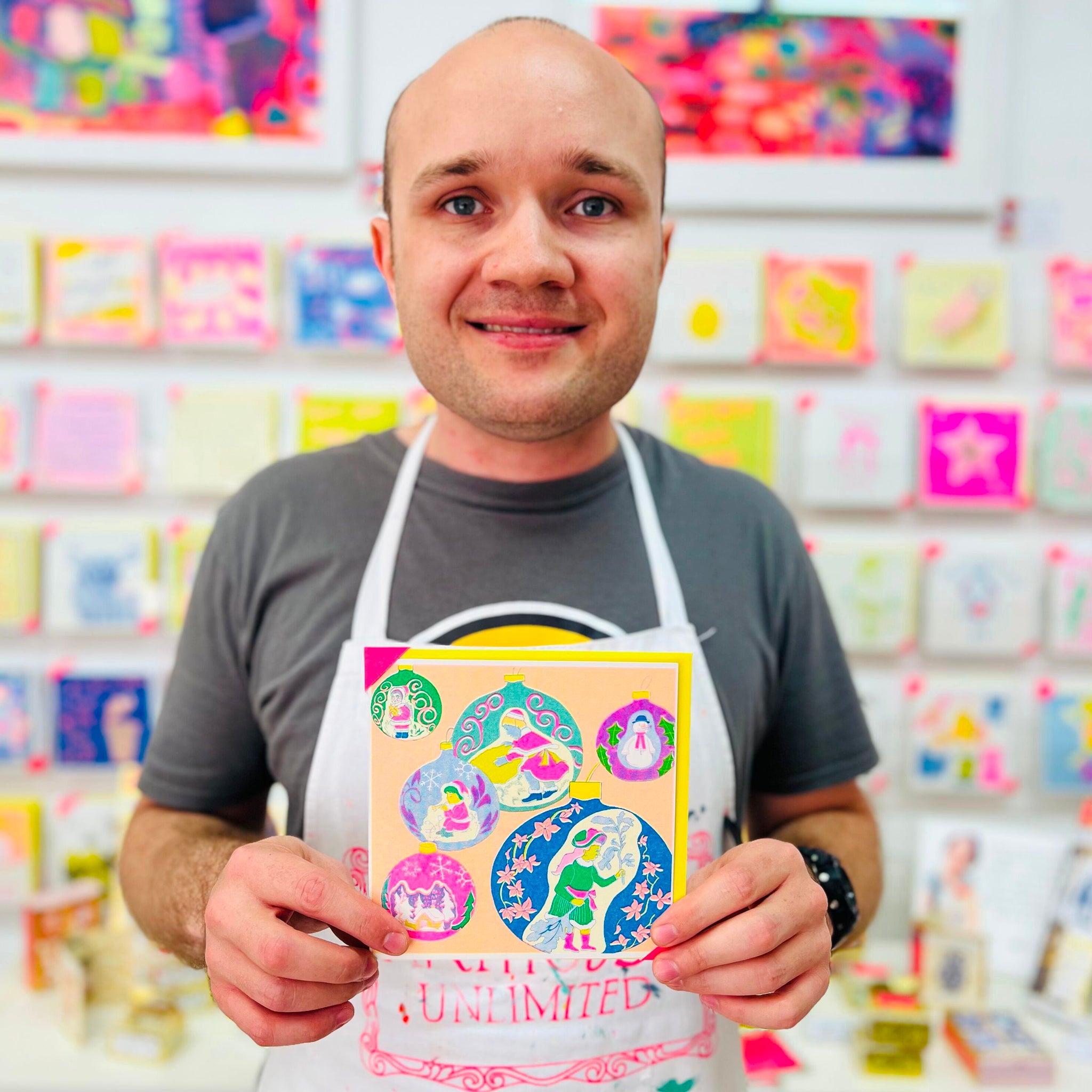 A male artist holding A bright coloured christmas card with hand drawn baubles