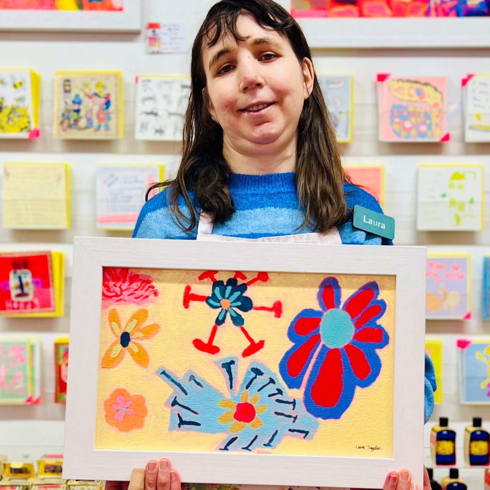 Female artist holding Framed painting of flowers in blues, purples and yellow