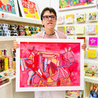 Male artist holding Framed bright coloured painting of several horses in pinks, blues and yellow
