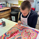 Male artist holding Framed painting of bright coloured strange creatures 