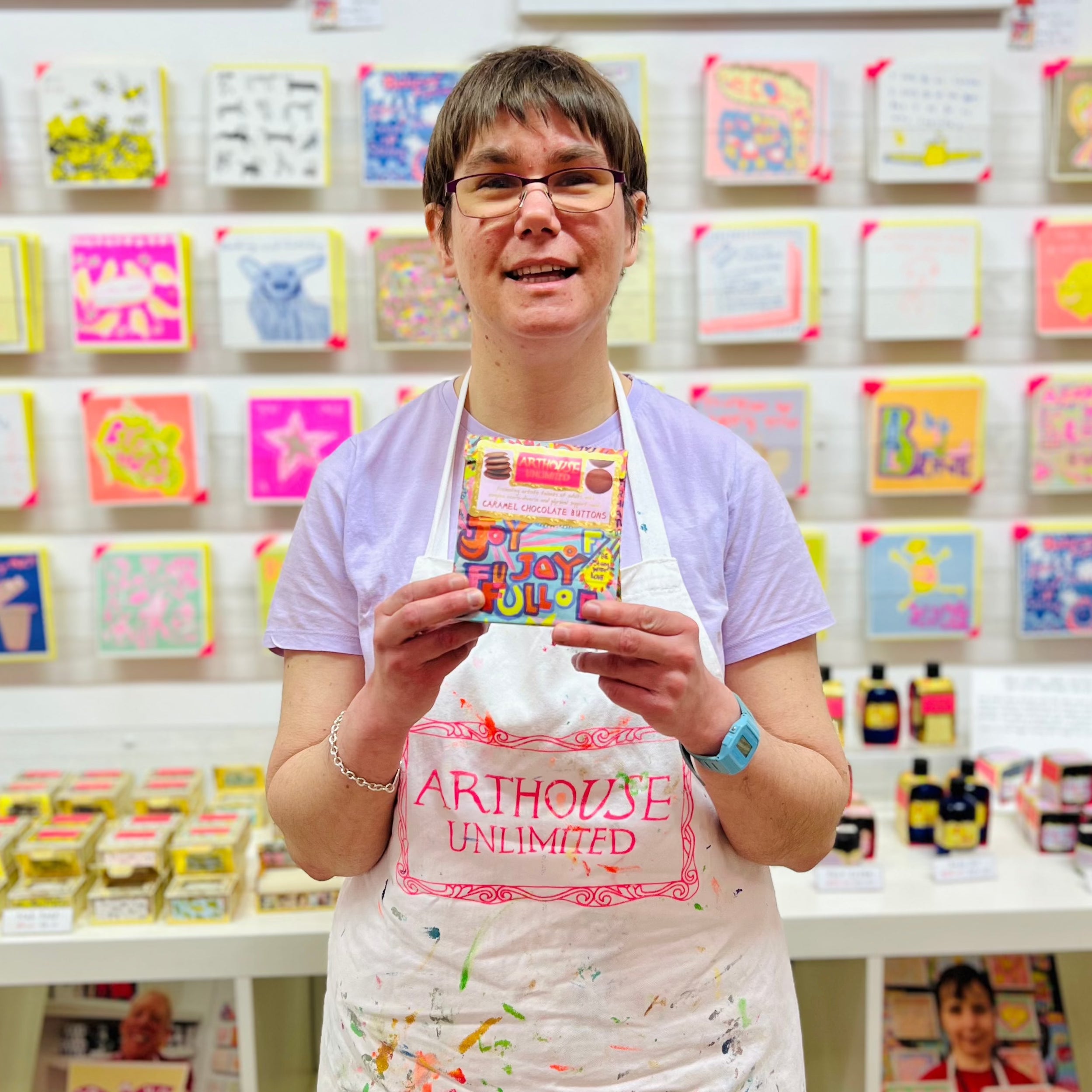 Female artist holding a packet of Bright and colourful packet of Full of Joy, Caramel Chocolate Buttons