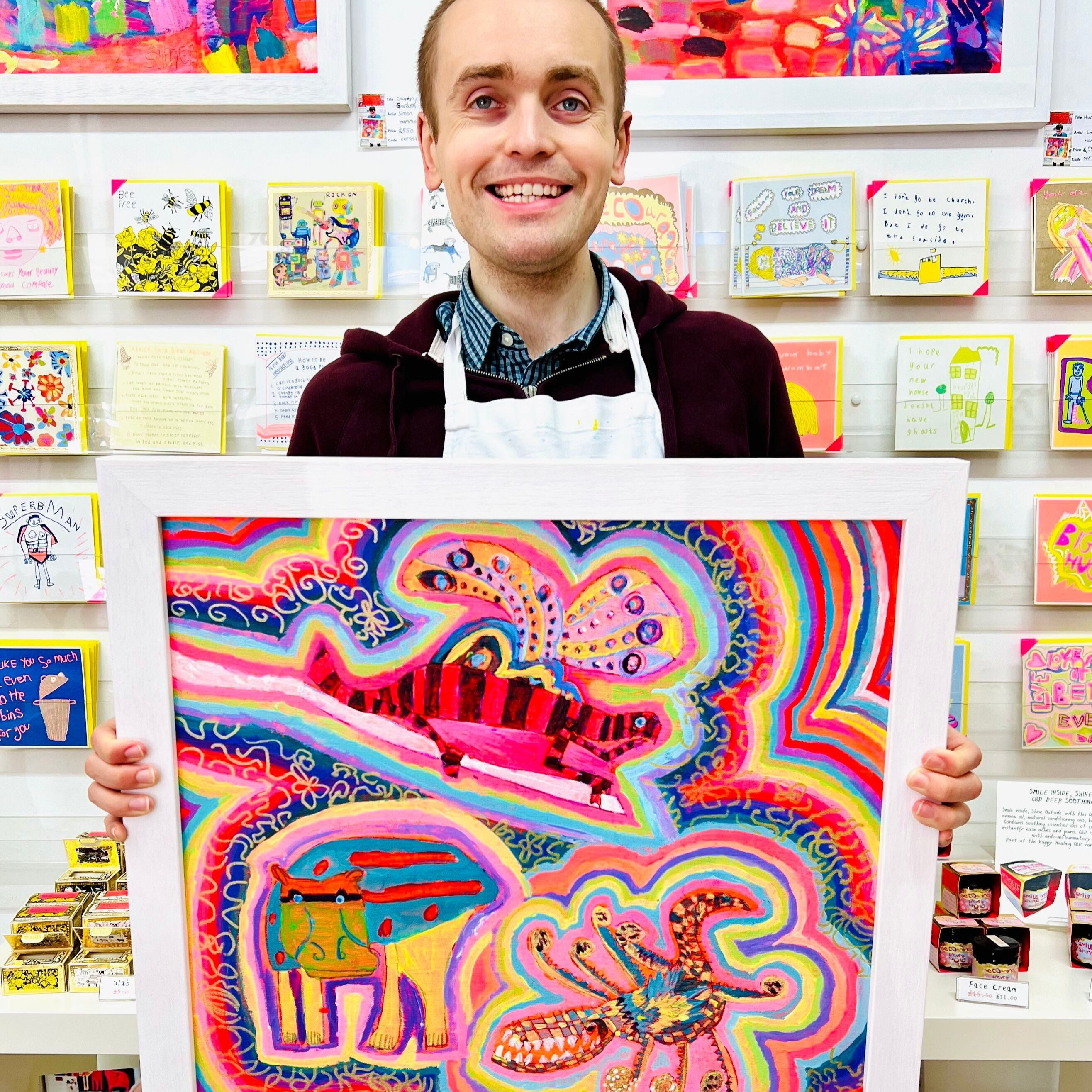 Male artist holding Framed painting of bright coloured strange creatures 
