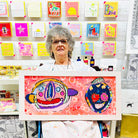 Female artist holding Framed colourful abstract painting of two characters in bright colours