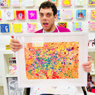 Male artist holding Framed colour painting of pink, orange and yellow splats