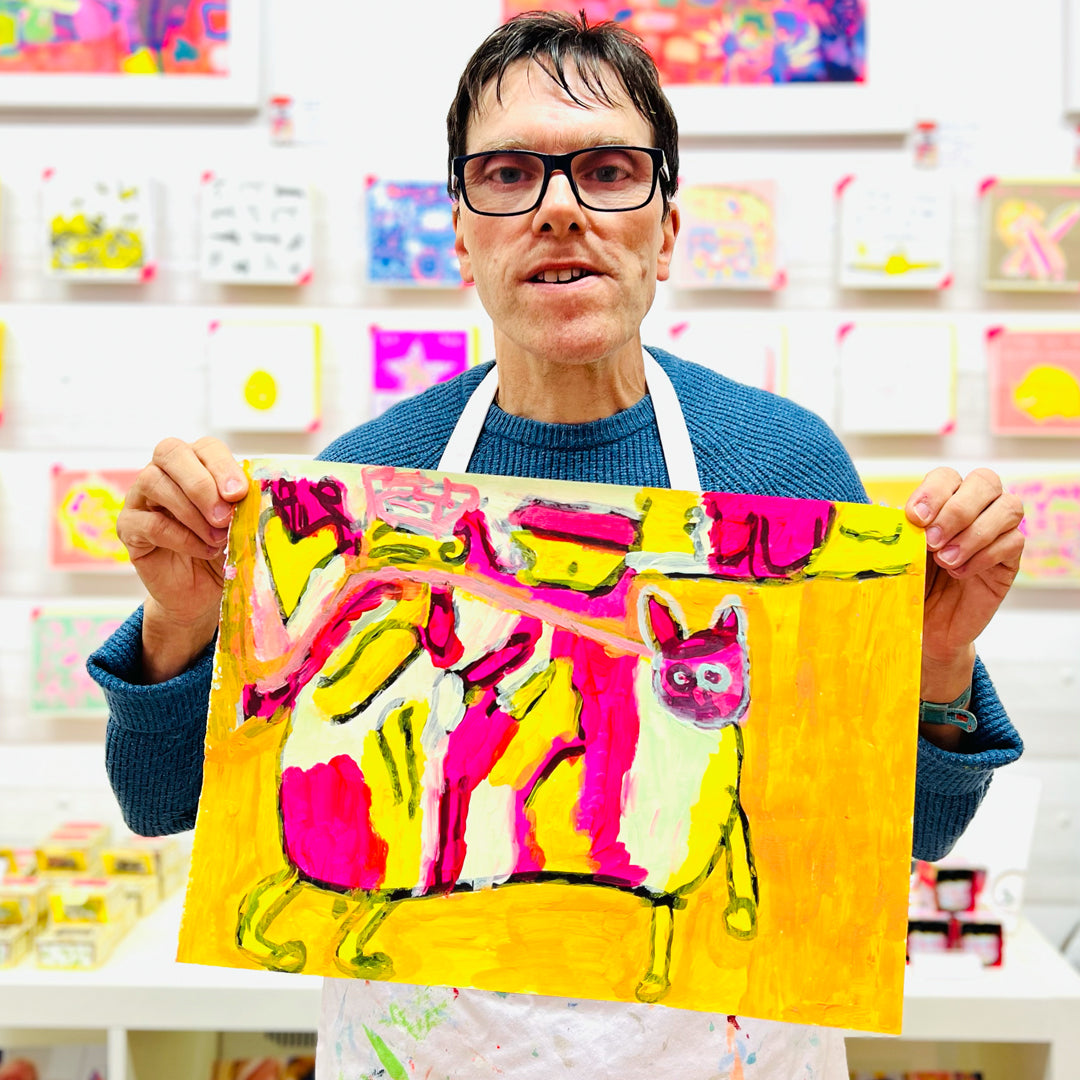 male artist holding Framed painting of a colourful cat in pink, green, orange and yellow